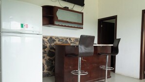 A kitchen area with a refrigerator, a stone backsplash, and two bar stools.