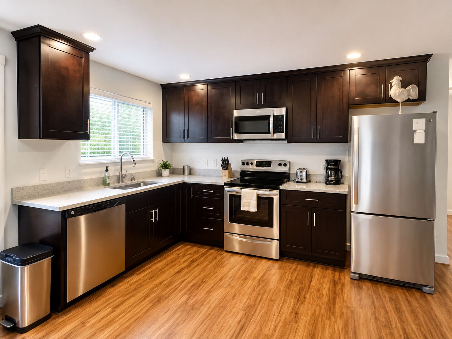 A modern kitchen with dark wood cabinets, stainless steel appliances, and a wooden floor.