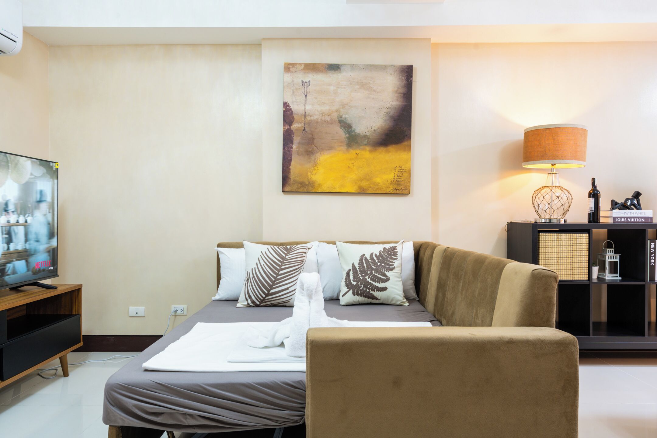 A modern living room with a sofa, a television, a painting, and a lamp.