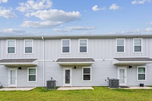 A row of three-story townhouses with a flat roof, white siding, and a front lawn. - Gulf Breeze 3BR Townhome | Pool & Playground | Near Zoo, Navarre Beach & Pensacola (Gulf Breeze)