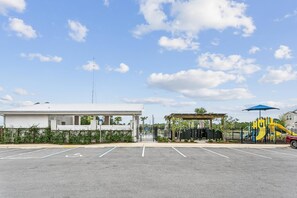 Un estacionamiento con entrada porticada, una zona de juegos techada y un edificio de fachada blanca.