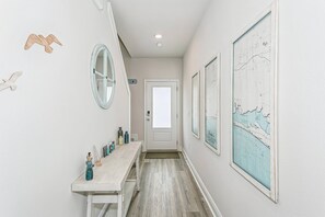 A hallway with a wooden bench, a door, and wall-mounted mirrors and maps. - Gulf Breeze 3BR Townhome | Pool & Playground | Near Zoo, Navarre Beach & Pensacola (Gulf Breeze)