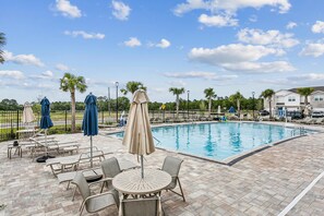 A swimming pool area with lounge chairs and umbrellas, surrounded by a fence and palm trees. - Gulf Breeze 3BR Townhome | Pool & Playground | Near Zoo, Navarre Beach & Pensacola (Gulf Breeze)