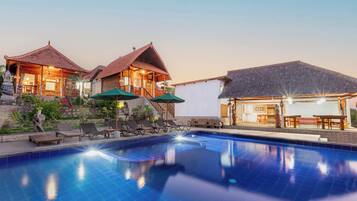 A resort with a swimming pool, lounge chairs, and a dining area.