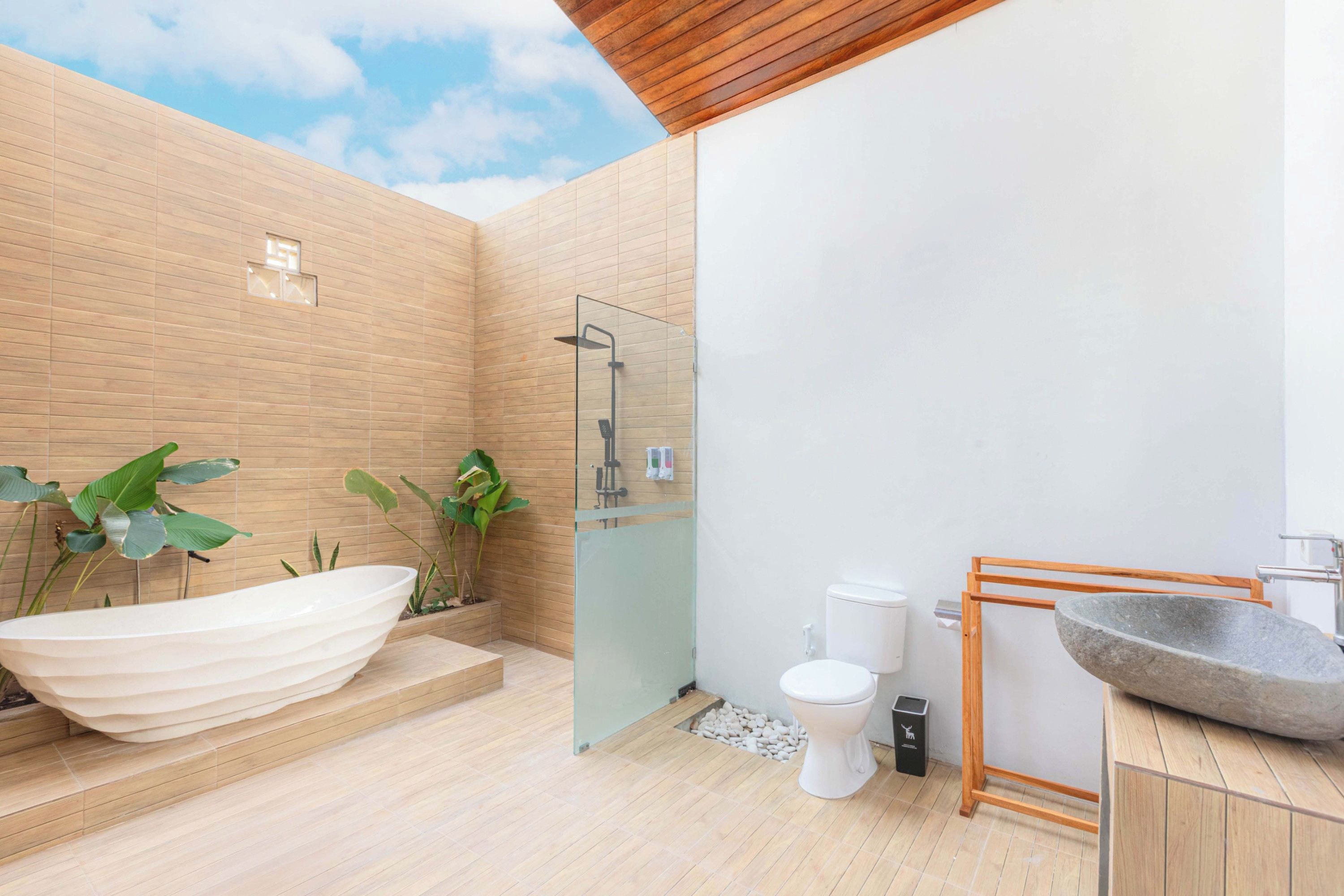 Un baño moderno con una bañera independiente, ducha con mampara de cristal, inodoro y lavabo de piedra.
