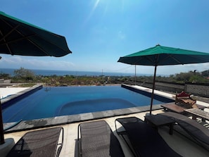 A swimming pool with lounge chairs and umbrellas, overlooking a scenic view. - Miyasabiasa Hills Nusa Penida (Klungkung)