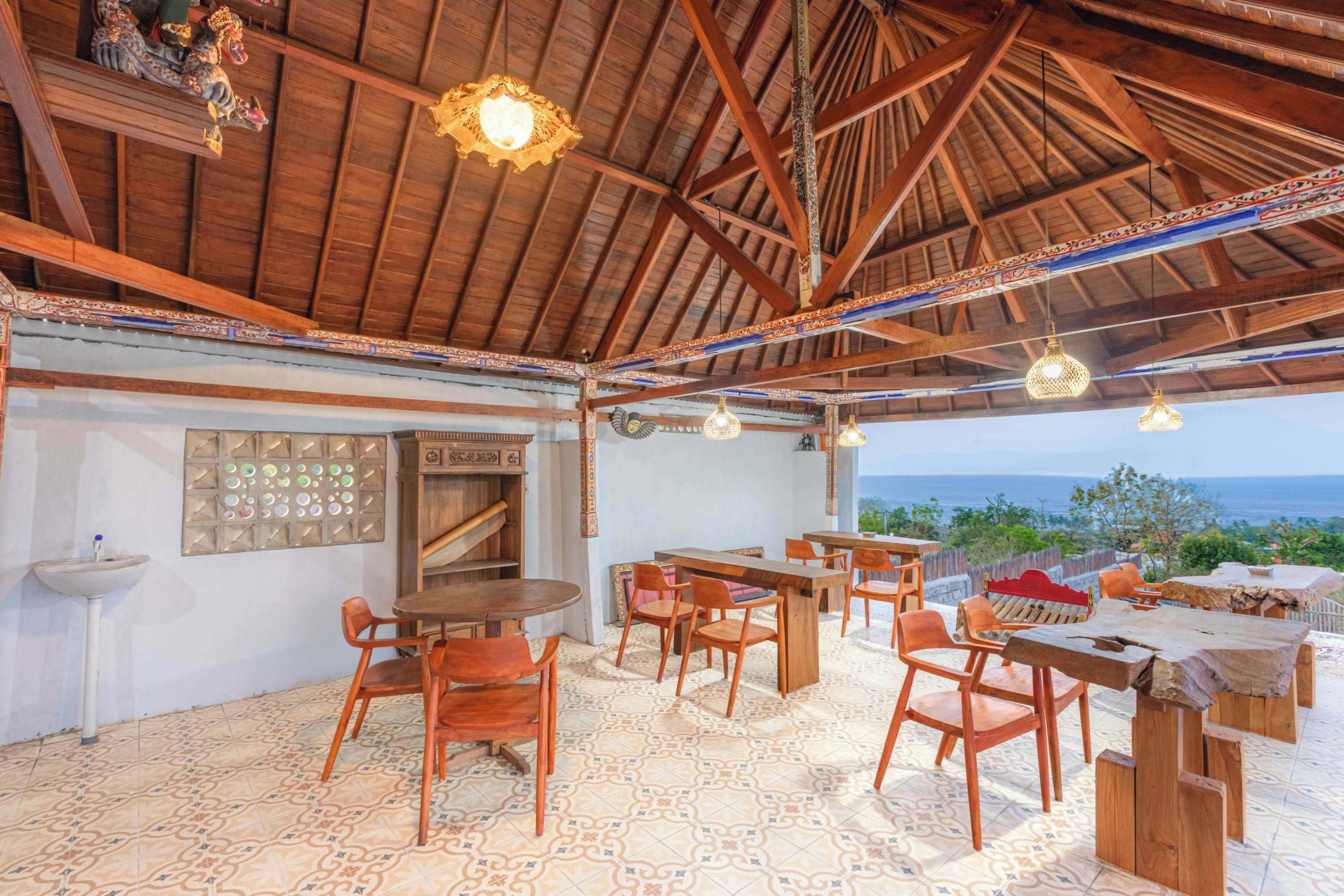 Un espacio de comedor al aire libre con mesas y sillas de madera, un muro decorativo y vista al océano.