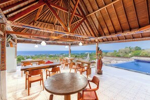Un área de estar al aire libre con mesas y sillas de madera, una estatua decorativa y vista al océano.