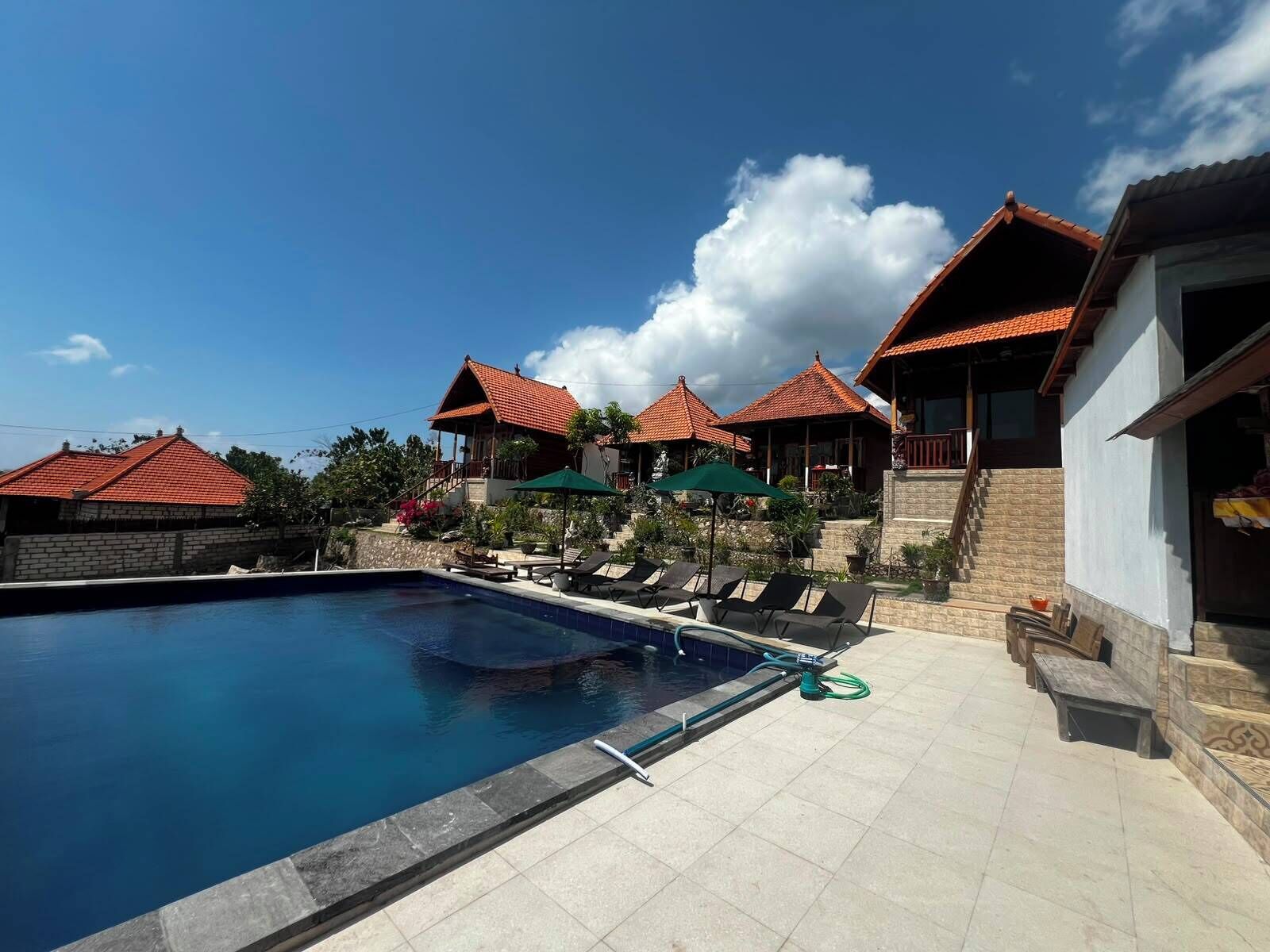 Un área de piscina con sillones de descanso, cielo despejado y edificios con tejados rojos.
