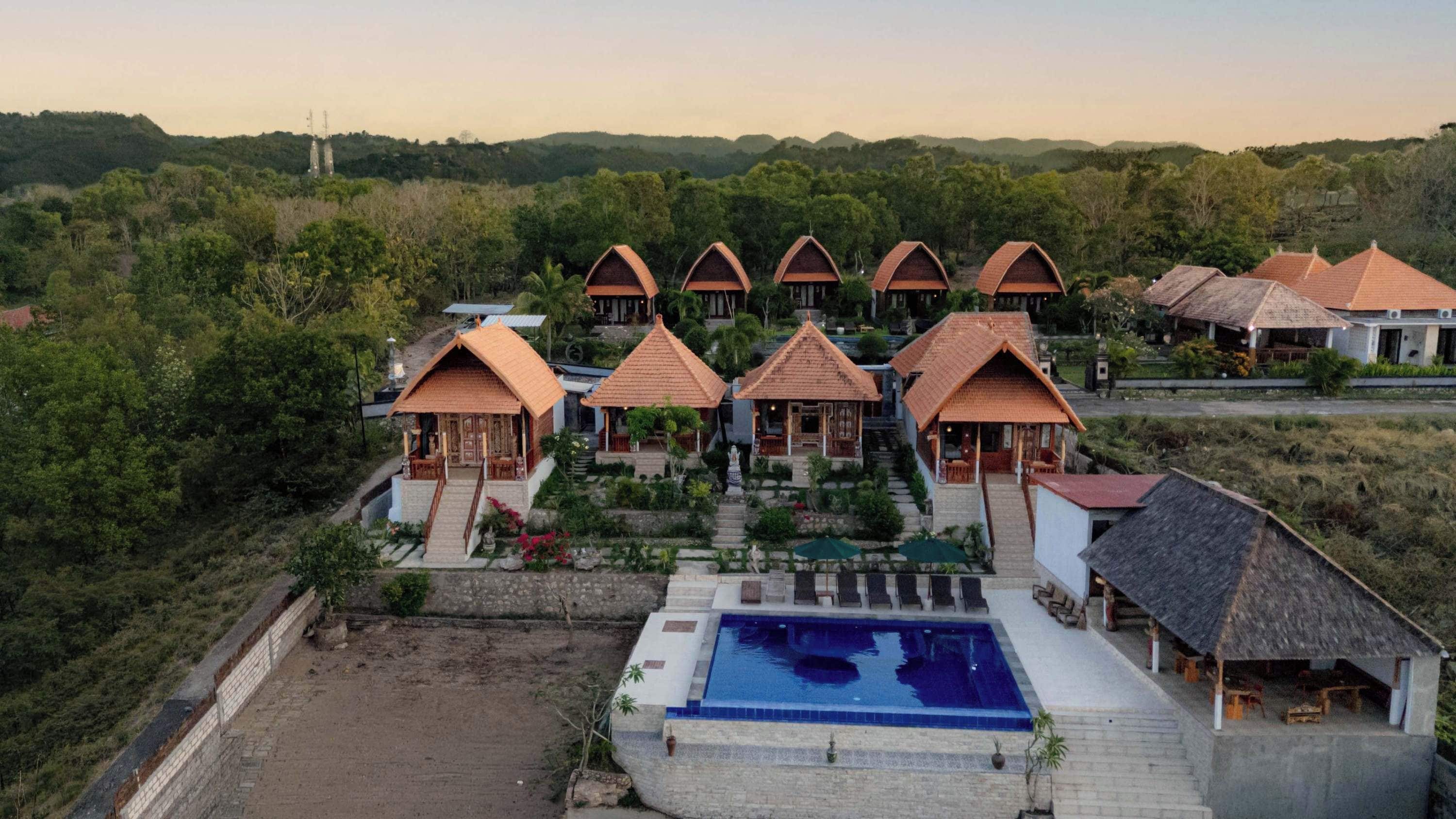 Un complejo turístico con varias cabañas, una piscina central y un paisaje exuberante y verde.
