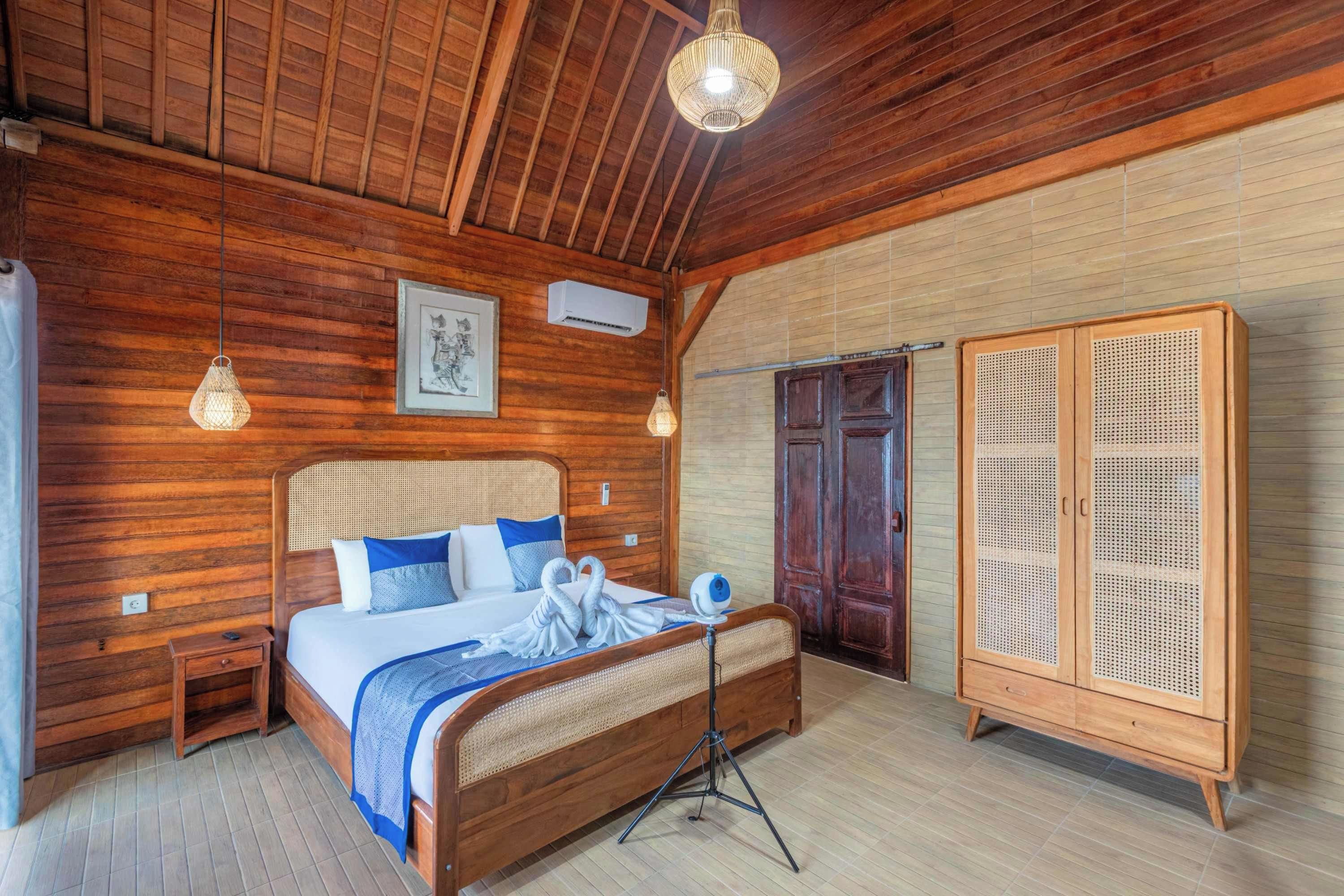 Una habitación de madera con una cama, mesitas de noche, un armario y una lámpara colgante.