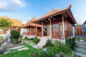 Una casa tradicional de madera con techo de tejas, un porche con barandillas de madera y un jardín con piedras y plantas.