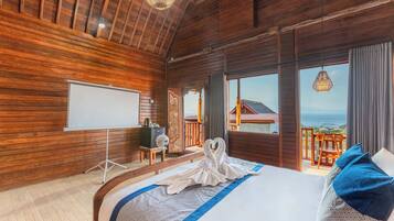 Quarto de madeira com cama, um quadro branco e vista para o mar.