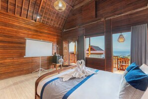 Quarto de madeira com cama, um quadro branco e vista para o mar.