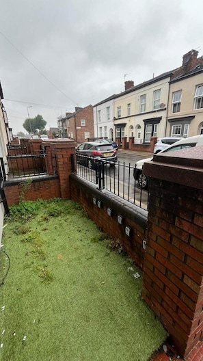 Una calle residencial con casas adosadas, un área verde y coches aparcados.