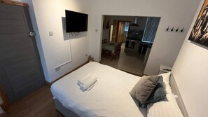 A hotel room with a bed, a flat-screen TV mounted on the wall, a small table with chairs, and a view into the kitchen area. - Anfield Apartment Sleeps 2 With Garden (Liverpool)