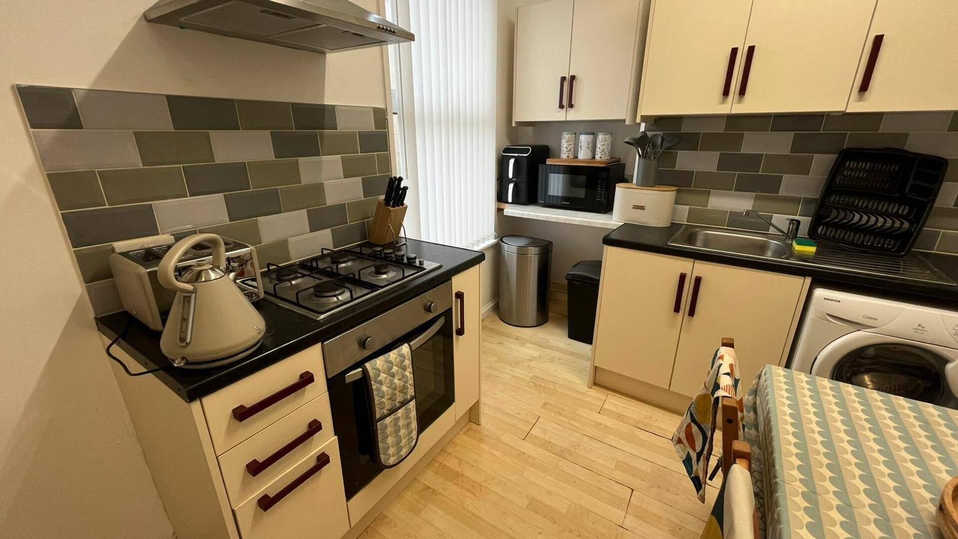 A compact kitchen with a gas stove, a kettle, a microwave, and a washing machine.