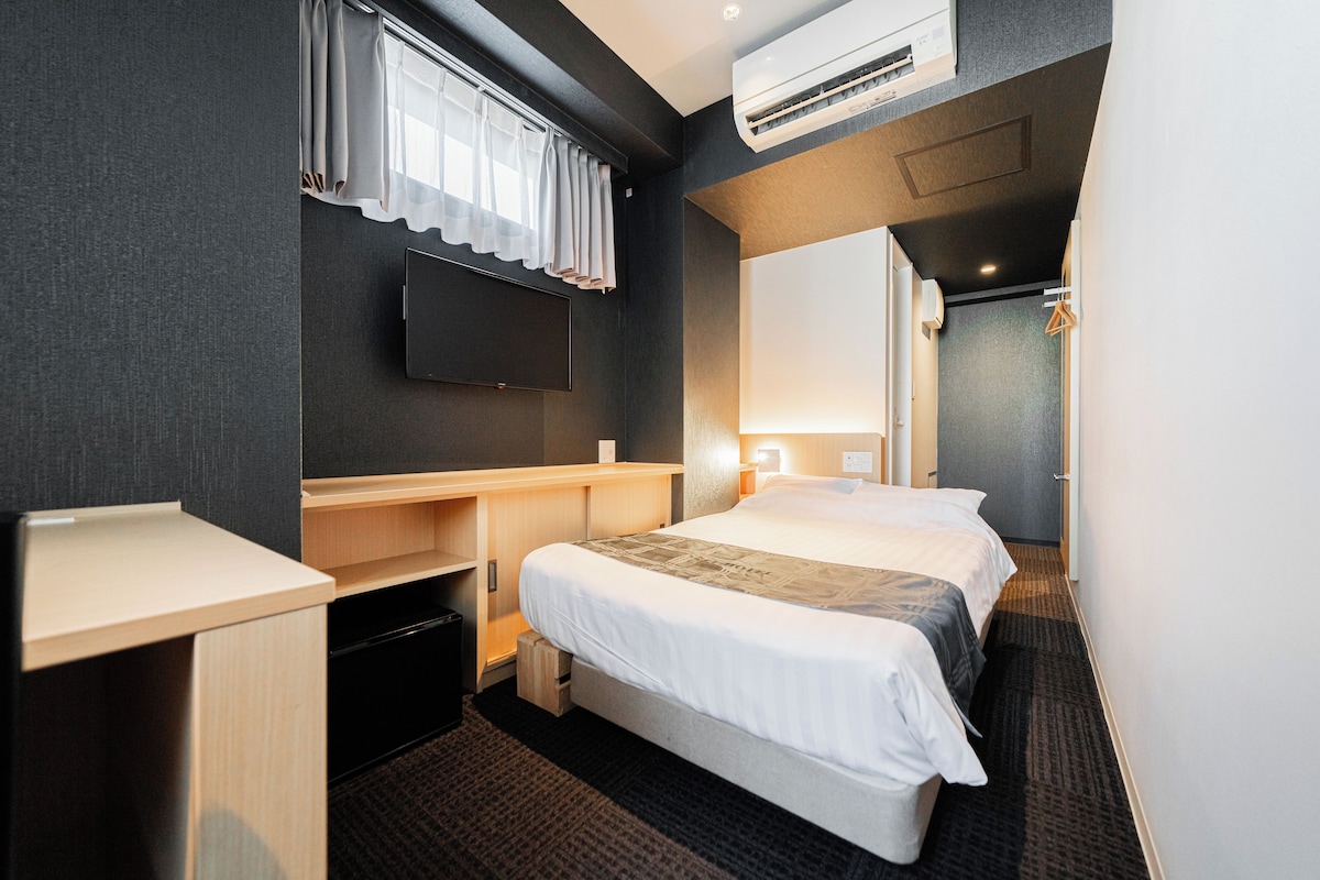 A hotel room with a bed, a desk, a TV, and an air conditioning unit.