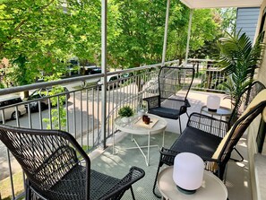 Ein Balkon mit Gartenmöbeln, darunter Stühle und ein Tisch, mit Blick auf eine Straße mit parkenden Autos und Bäumen.