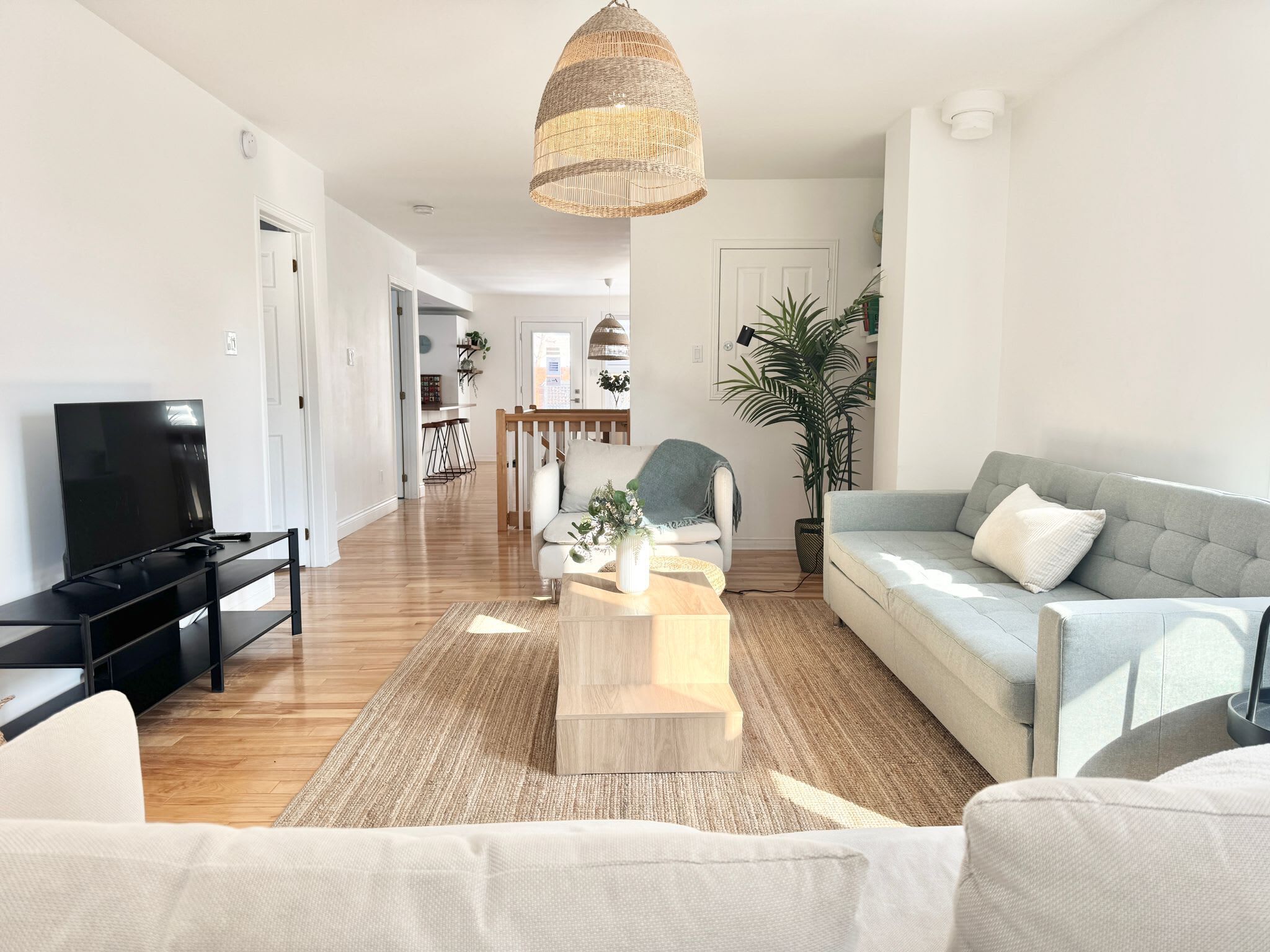 Un salon moderne avec un téléviseur à écran plat, un canapé gris, un fauteuil blanc et une table basse.