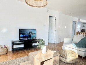 Ein modernes Wohnzimmer mit Flachbildfernseher, einer Couch, einem Couchtisch und einem Korbwägelchen.
