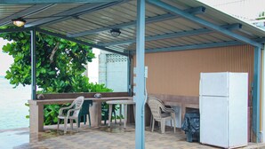 A covered outdoor seating area with a table and chairs, a refrigerator, and a view of the water. - Beachfront home with beautiful sunset views. Must see! (Asan)