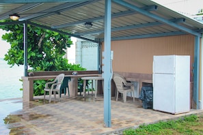 A covered outdoor seating area with a table and chairs, a refrigerator, and a view of the water. - Beachfront home with beautiful sunset views. Must see! (Asan)