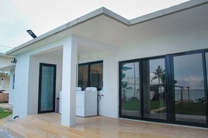 A modern building with a covered patio area, a washing machine, and a large sliding glass door. - Beachfront home with beautiful sunset views. Must see! (Asan)