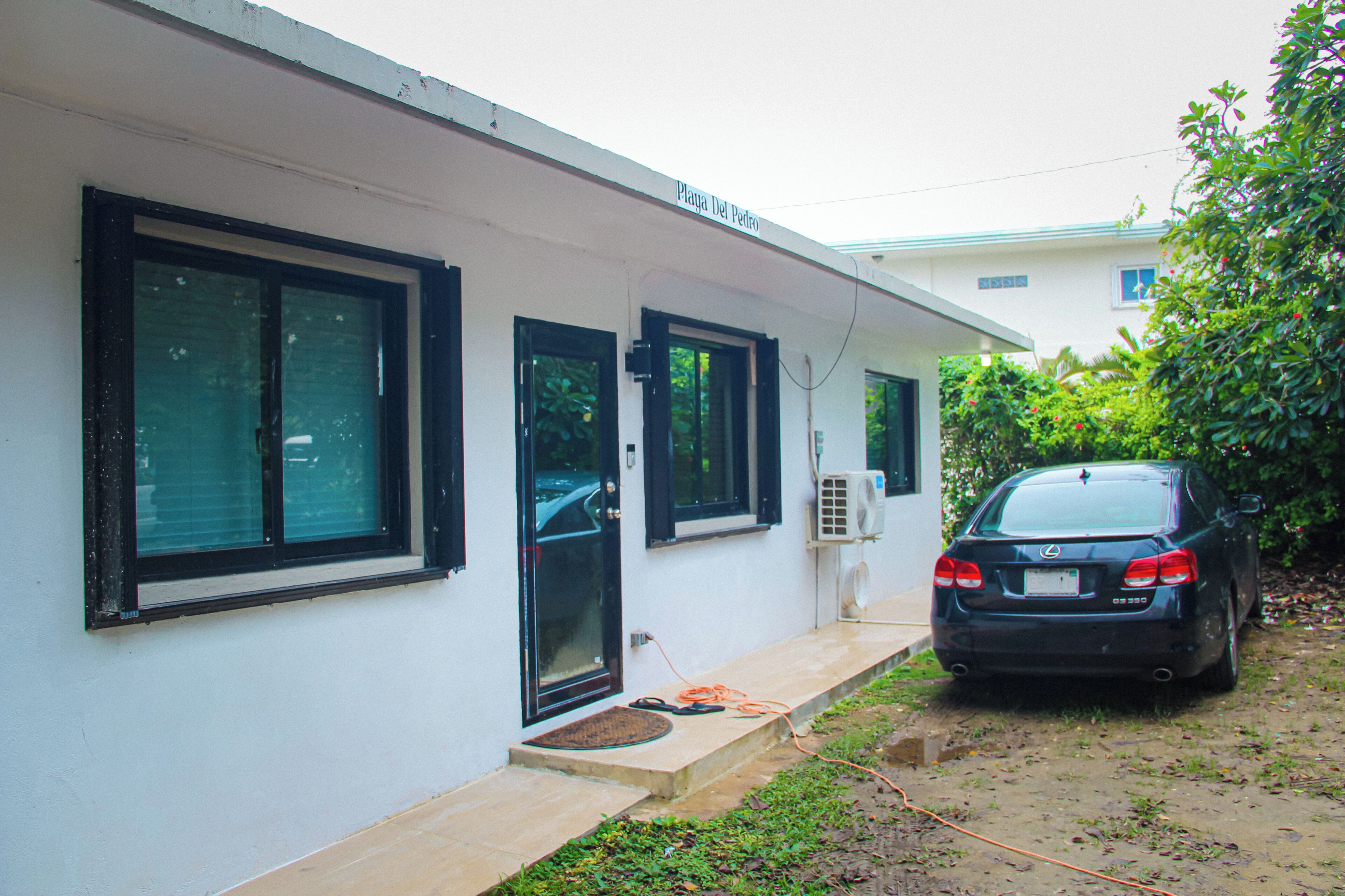 A single-story building with a white exterior, large windows, and a car parked in the driveway.