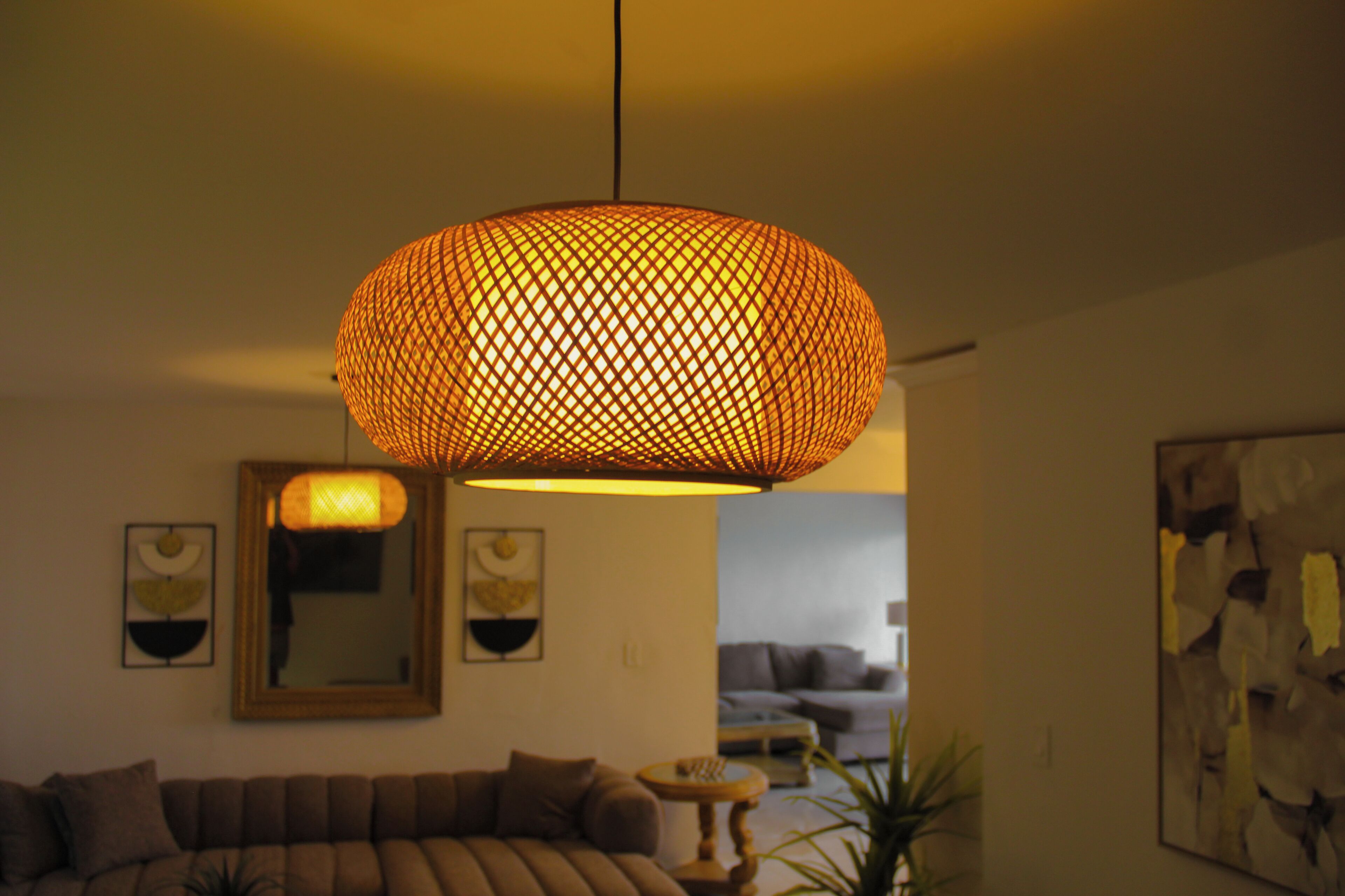 Un salon avec un grand luminaire suspendu en fibres tressées, un canapé, une petite table ronde et un tableau accroché au mur.
