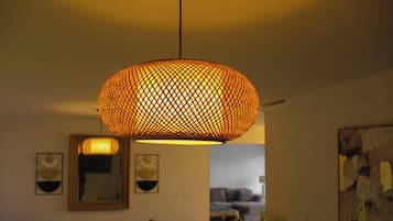 Un salon avec un grand luminaire suspendu en fibres tressées, un canapé, une petite table ronde et un tableau accroché au mur.