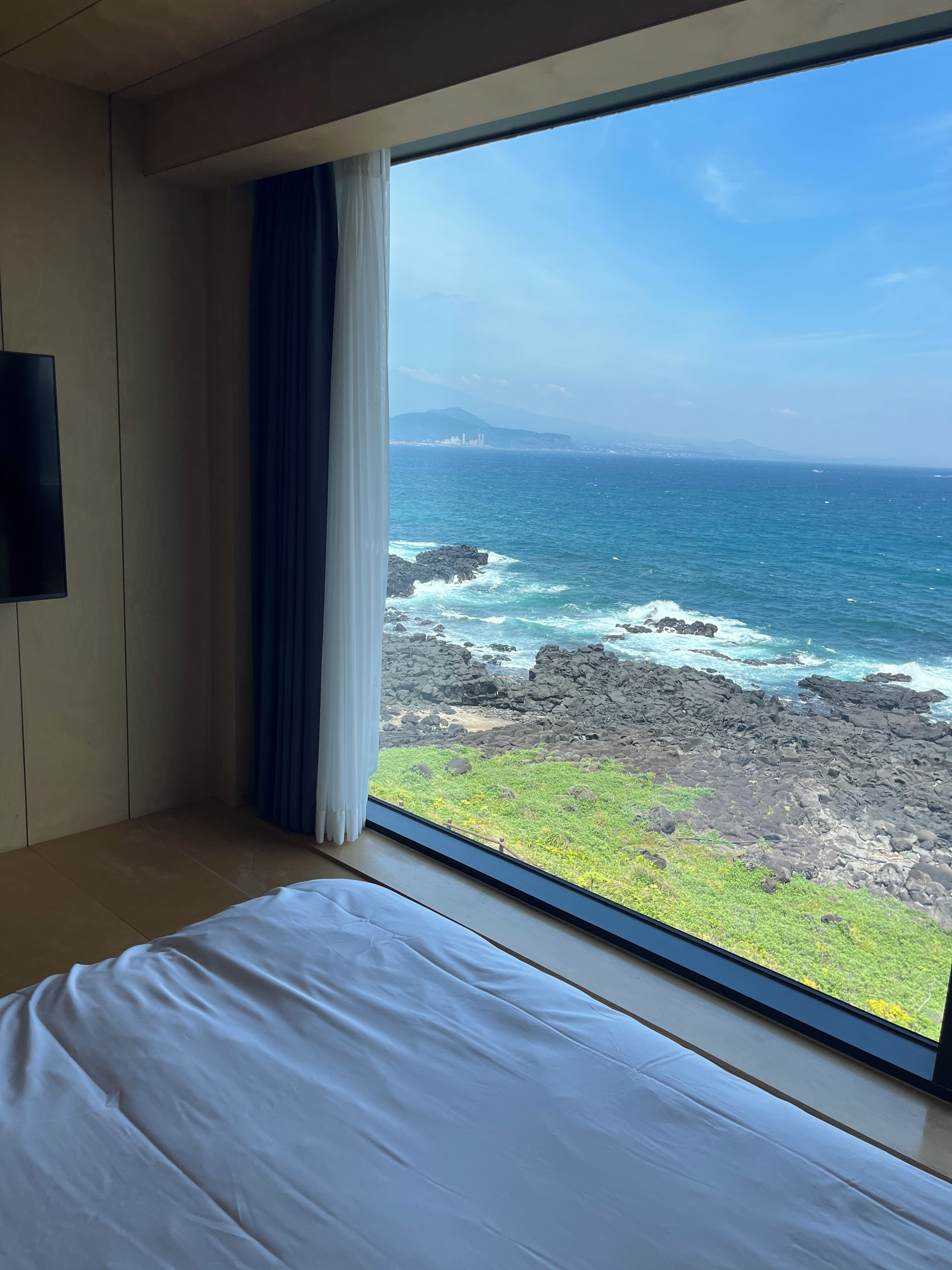 A room with a bed and a large window overlooking a rocky coastline and ocean.