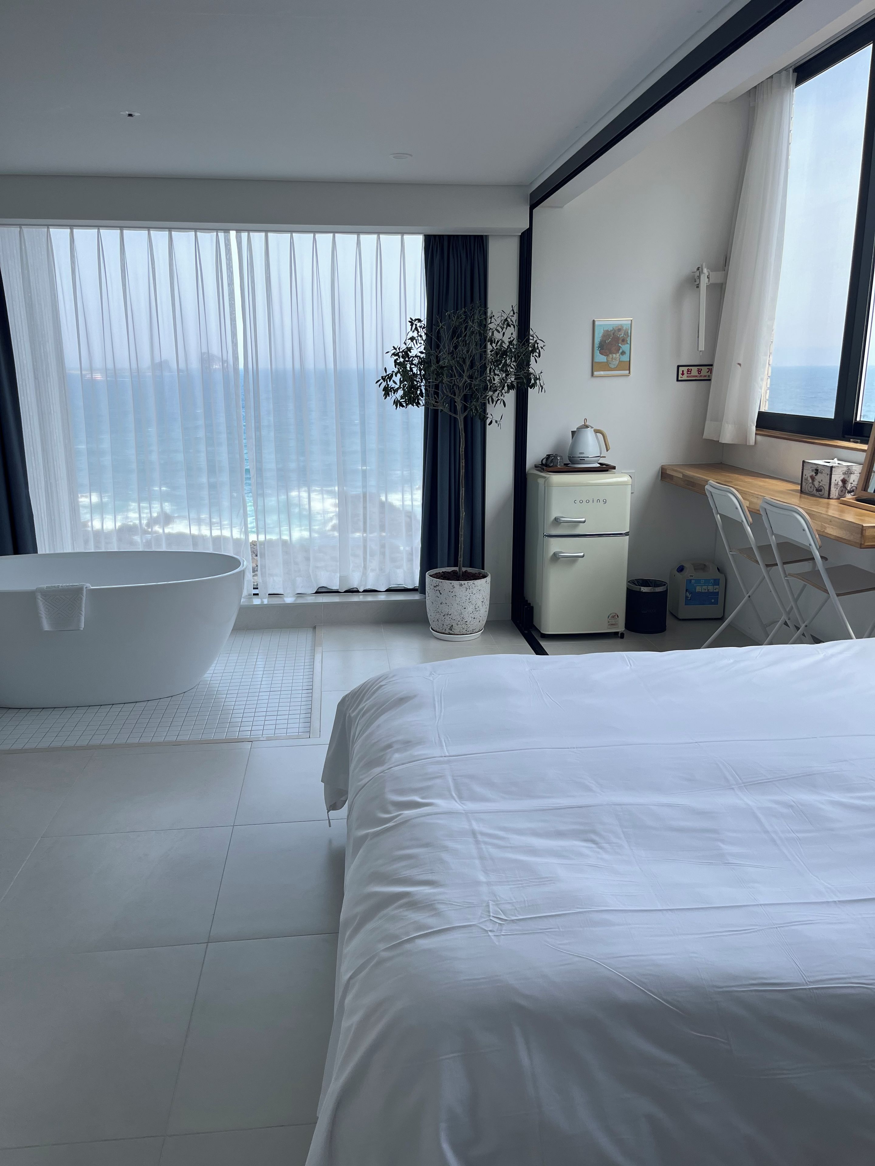 Un dormitorio moderno con una cama grande, una bañera, una planta en maceta y vistas al océano.