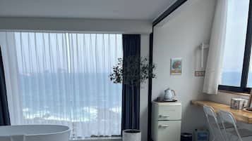 Un dormitorio moderno con una cama grande, una bañera, una planta en maceta y vistas al océano.