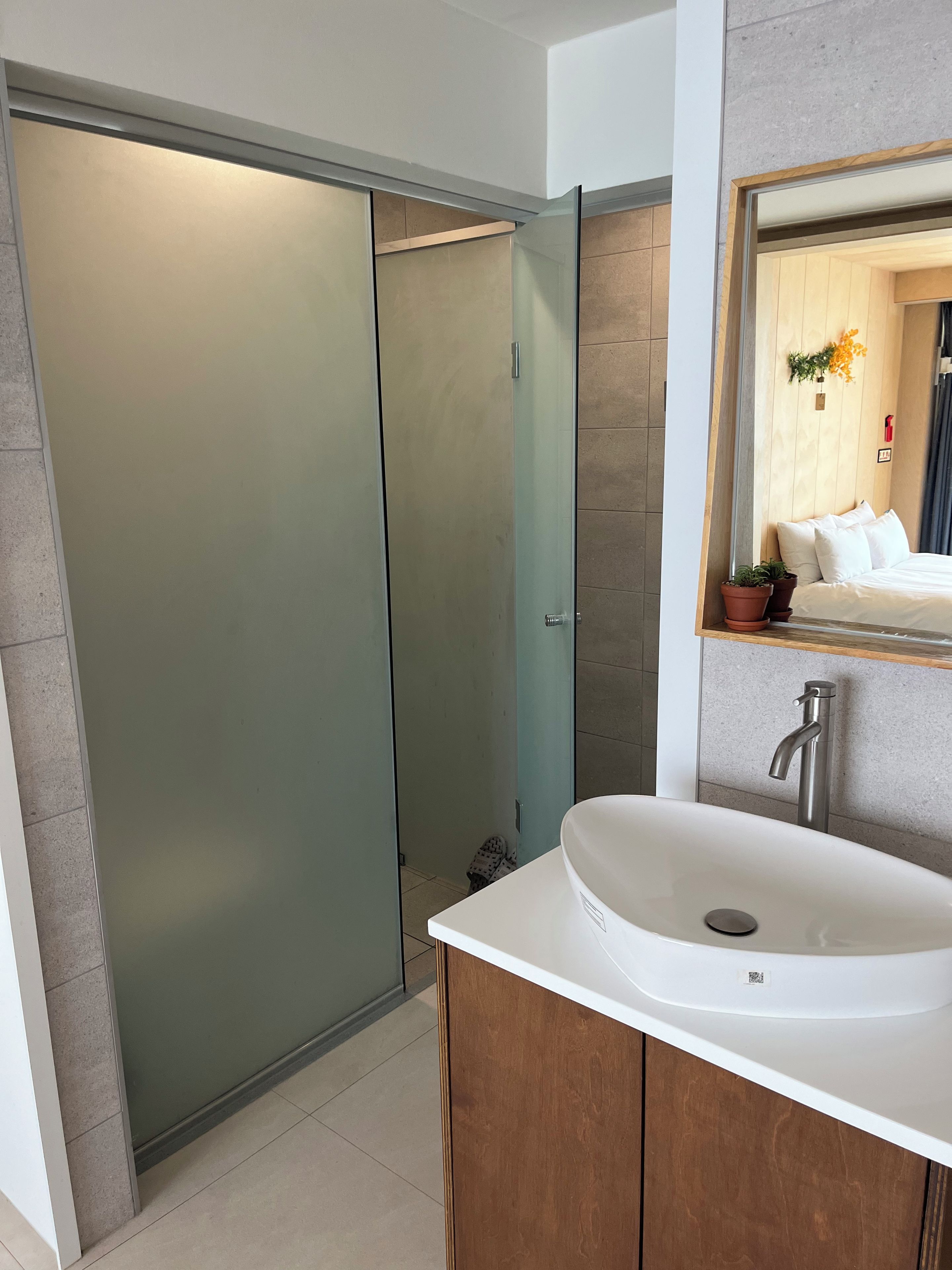 Ein modernes Badezimmer mit einer Duschkabine aus Glas, einem weißen Waschbecken mit einem Einhebelhahn und einer Holzwaschkommode.