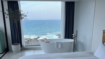 Une chambre avec un grand lit, une baignoire et une vue sur l’océan.