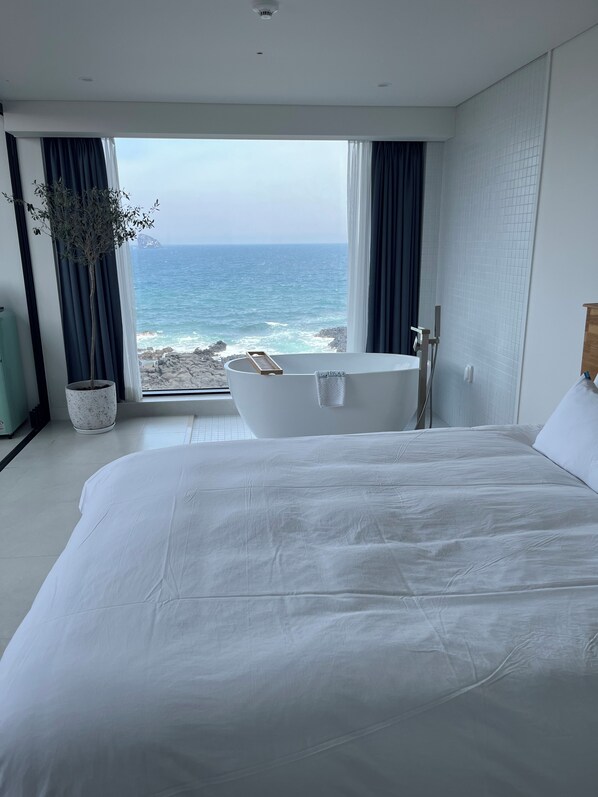 Un dormitorio con una cama grande, una bañera y vistas al océano.