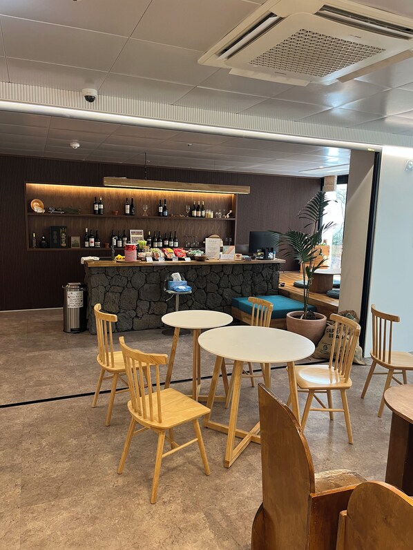 A bar area with multiple shelves of bottles, a stone counter, and several wooden chairs and tables.