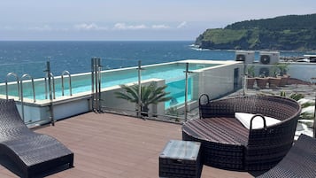 Una terraza en la azotea con piscina, sillas de descanso y vistas al océano.