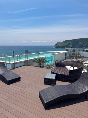 A rooftop terrace with a pool, lounge chairs, and a view of the ocean.