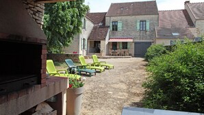 Ein Garten mit Grill, Sitzgelegenheit im Freien und Blick auf ein zweistöckiges Haus.