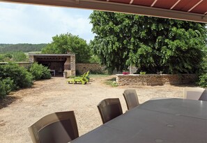 Un patio al aire libre con una mesa, sillas, una estructura de piedra y un árbol grande.