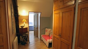 Ein schmaler Flur mit Heizkörper, einem Tisch mit Lampe, einem Bett mit Blumenmuster und Holzschränken.