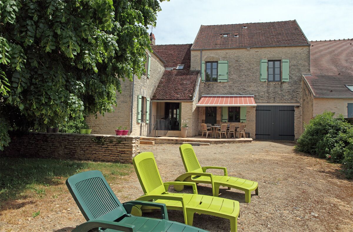 Een huis met een gevel van natuursteen, een pannendak en een patio met groene stoelen en een tafel.