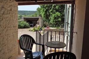 An outdoor seating area with a table and chairs, a view of a stone building, and greenery in the background.