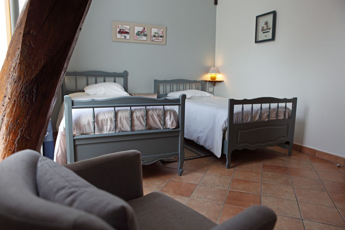 Une chambre avec deux lits, une chaise et un mur décoré de tableaux.