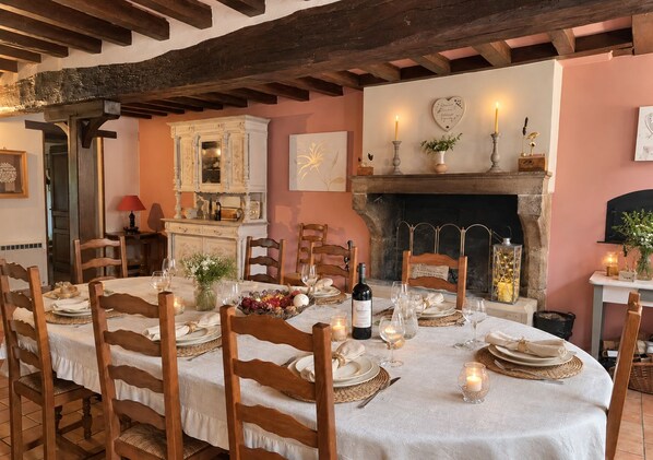 Comedor con una mesa redonda dispuesta para una comida, sillas de madera, chimenea y un estante con adornos.