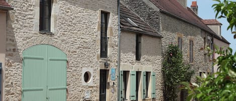 Une rangée de bâtiments en pierre, avec des volets verts et une porte verte.