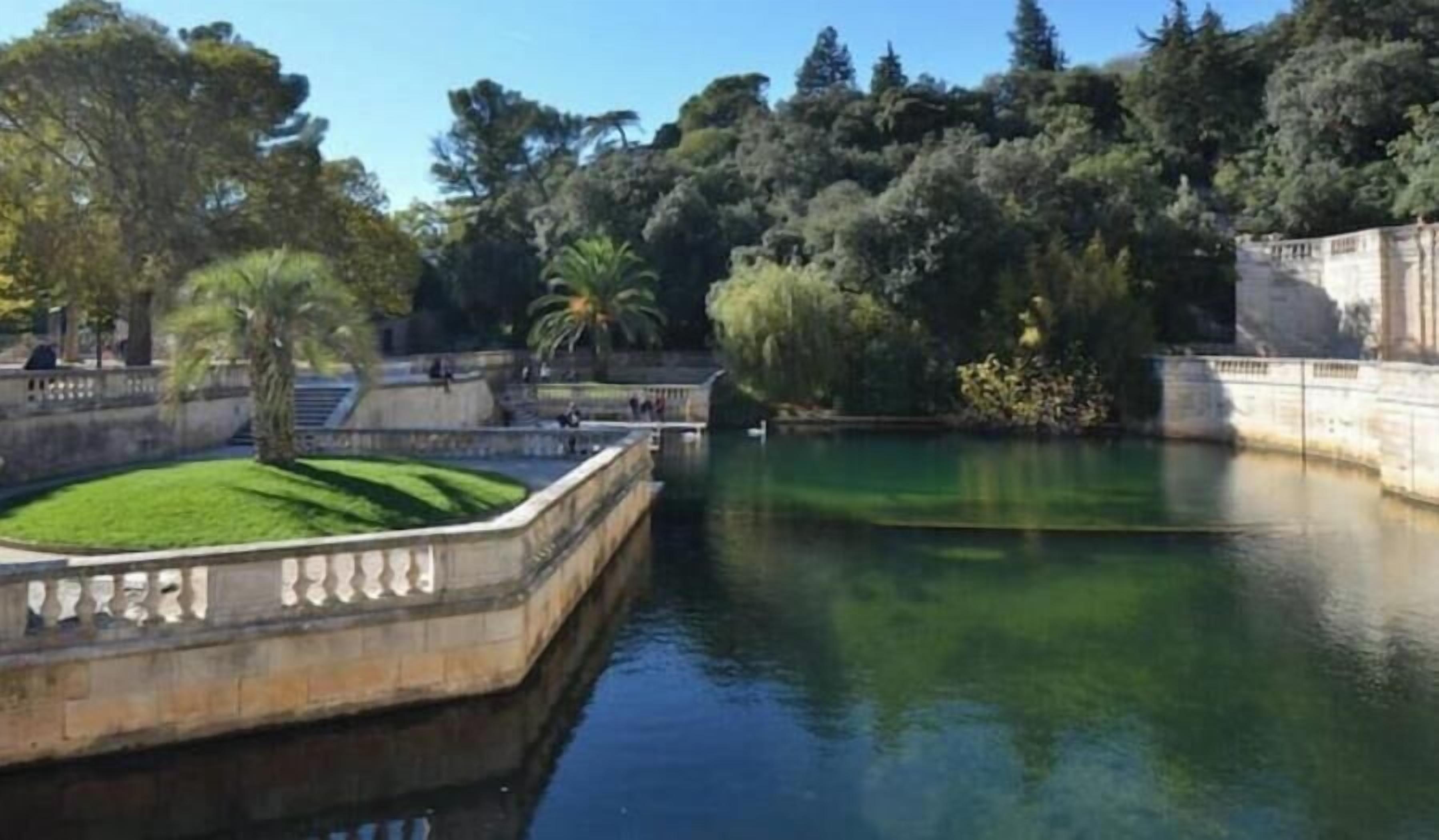 Um corpo d'água calmo com uma ponte de pedra, vegetação exuberante e céu claro.
