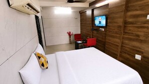 A hotel room with a bed, a TV mounted on the wall, and a red chair. - Hotel Vatsalya (Rajkot)